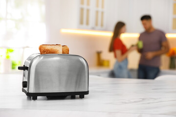 Modern toaster with slices of bread and blurred couple on background