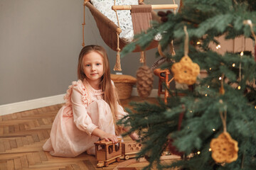 Little girl in pink dress playing in christmas interior