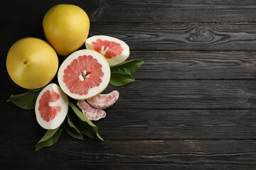 Fresh cut and whole pomelo fruits on black wooden table, flat lay. Space for text