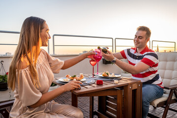 Beautiful young couple enjoying romantic dinner at roof top terrace drinking vine and eating food 
