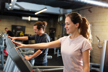Fototapeta na wymiar Young fit man and beautiful brunette exercising on the treadmill in modern fitness gym.