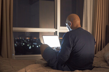 Happy smiling business, black man, African American people working from home and using computer notebook laptop with blank screen in quarantine on bed in bedroom at home at late night. Lifestyle