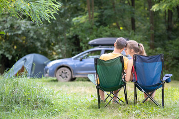 Happy couple sitting on chairs at campsite hugging each other. Travel, camping and vacations concept.