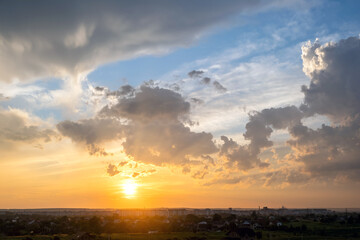 Dramatic sunset landscape of rural area with puffy clouds lit by orange setting sun and blue sky.