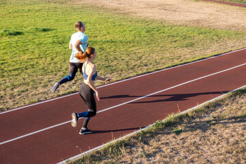 Young couple of fit sportsmen boy and girl running while doing exercise on red tracks of public...
