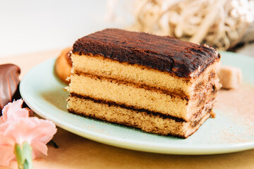 piece of cake with chocolate. A piece of tiramisu tart in a green plate. Zephyr with chocolate and small pink carnations	