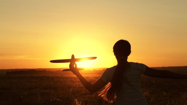 Free girl runs with toy airplane in her hand across field in rays of sunset. Child plays airplane. Teenager dreams of flying and becoming pilot. Kid wants to become pilot and astronaut. Slow motion