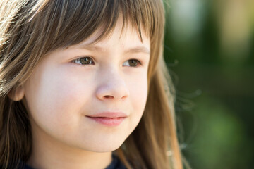 Portrait of pretty child girl with gray eyes and long fair hair outdoors on blurred bright background. Cute female kid on warm summer day outside.