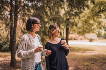 Two happy young women having coffee break together in park