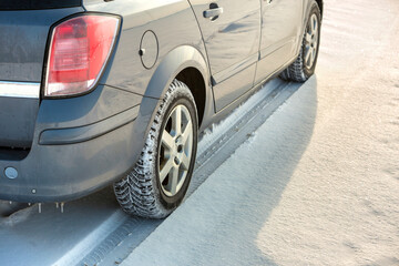 Fototapeta na wymiar Close up of a car tire parked on snowy road on winter day. Transportation and safety concept.