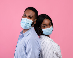 Valentine's Day during covid-19 pandemic. Black couple wearing face masks, standing back to back on pink background