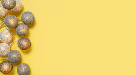 Gray white festive garland on yellow background flat lay top view. Cotton Balls Garland. Round bulbs LED festoon lights electric garland. Festive decoration Colors year 2021 Illuminating Ultimate gray
