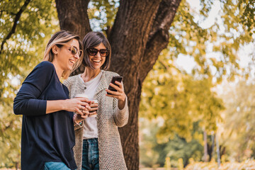 Two happy smiling women friends checking smart phone content in a park