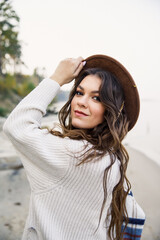 young beautiful girl in a white sweater, brown skirt and brown hat are walking on the coast  near the lake