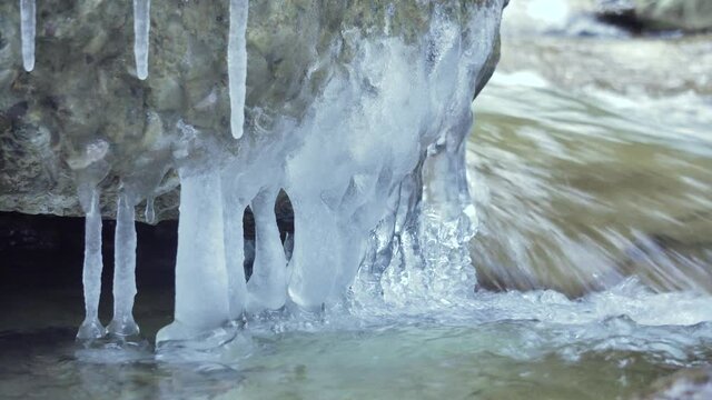 Close up of icicles in wild stream. Winter Creek. Cold slippery seasonal weather. Row of frosty icicles with Flowing Water