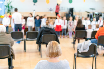 Parents at the performance of children in kindergarten or school. Children on stage. Many parents are watching the kids performance in the hall during Chistmas holiday, blurry