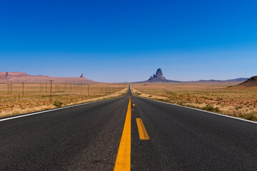 Fototapeta na wymiar Scenic view of the US highway 163 leading to the Monument Valley with sandstone buttes on the background; Concept for travel in the USA and road trip.