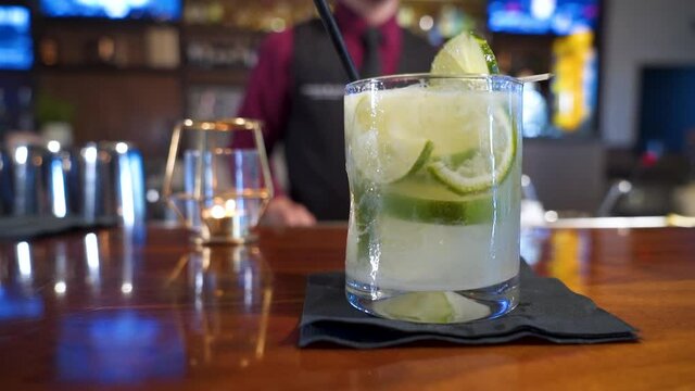 Bartender serves national drink of Brazil Caipirinha garnished with limes, slider close up slow motion 4K