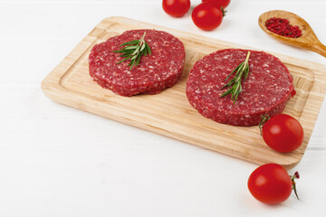 Two raw beef burger patties on wooden board