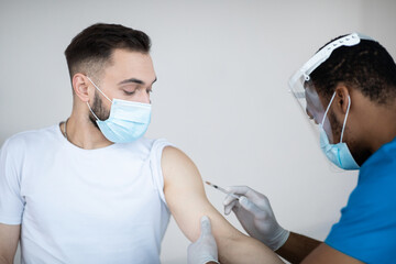 Fototapeta na wymiar Young Caucasian man getting injection of coronavirus vaccine at hospital. Healthcare and global infection prevention