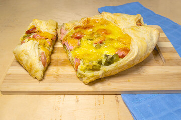 Puff pastry pie with tomatoes, pine, pickles cut on a wooden cutting board