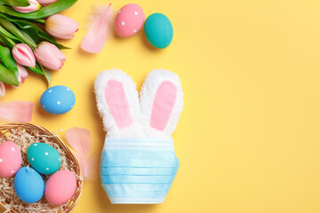 Easter concept. Rabbit in a protective medical mask and a basket with colored eggs on a yellow background.