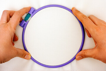 Plastic embroidery hoop with white cross stitch fabric in woman hands