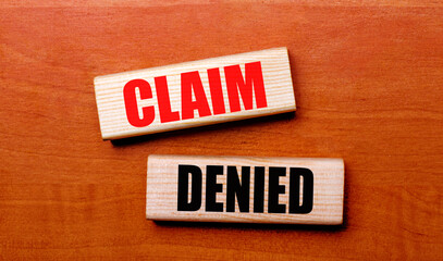 On a wooden table are two wooden blocks with the text CLAIM DENIED