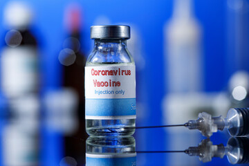 filetta di vetro del vaccino anti-covid  con una siringa e posti sulla superfice riflettente del tavolo di un  laboratorio, isolati  su sfondo blu