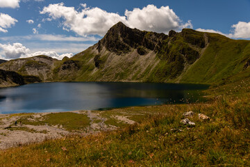 Fanealm und Wilder See in Suedtirol, Italy, Alpine pastures with a deep blue lake, green meadows and a blue sky with fleecy clouds, in summer