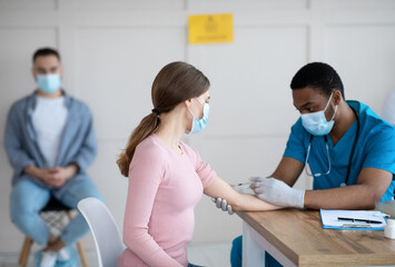 African American doctor injecting covid-19 vaccine to young woman at clinic. Immunization against global virus