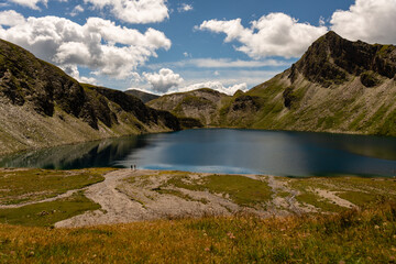 Naklejka na ściany i meble Fanealm und Wilder See in Suedtirol, Italy, Alpine pastures with a deep blue lake, green meadows and a blue sky with fleecy clouds, in summer