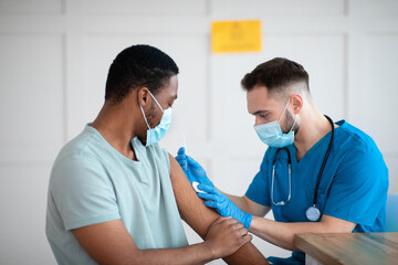 African American man in face mask receiving coronavirus immunization, taking shot of covid-19 vaccine at medical office