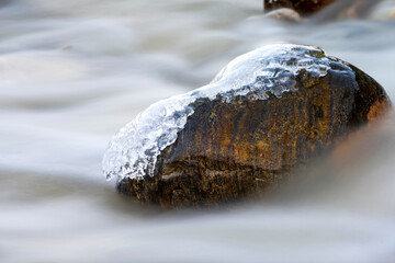 Ice covered rocks laying in shallow brook during an cold winter day, long exposure