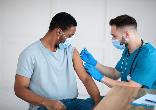 Medical doctor or nurse giving coronavirus vaccine shot to African American male patient at clinic