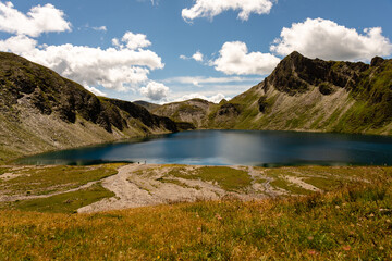 Fototapeta na wymiar Fanealm und Wilder See in Suedtirol, Italy, Alpine pastures with a deep blue lake, green meadows and a blue sky with fleecy clouds, in summer