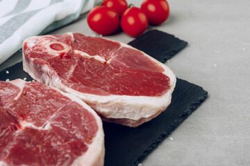 Raw rib-eye beef steak on wooden cutting board on gray background