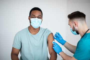 Immunization and health care system. Black male patient visiting doctor, receiving covid-19 vaccine...