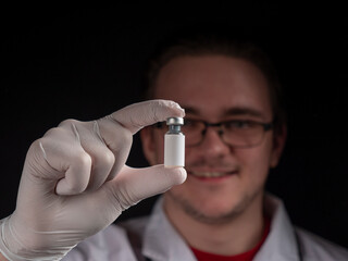 A young doctor holds a glass vial in which the liquid is with a vaccine.