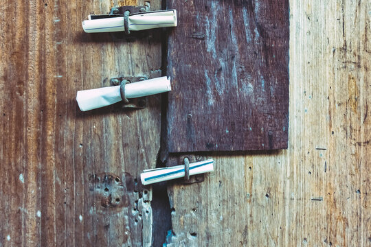 Three Small Rolls Of White Papers Notification Inserted Into Old Rusty Padlock Hasp On The Old Wooden Door. Bulletin Sticking Out At The Gate Of The Abandoned House. Selective Focus.