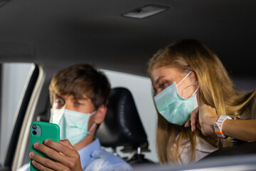 Caucasian young woman wearing protective face mask traveling with taxi and man driver. 