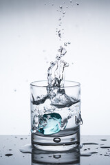 Splash of ice in a glass of water, ice falls into water, closeup