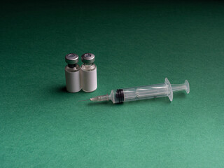 Two glass vials in which a liquid with a vaccine stand a syringe lies next to it