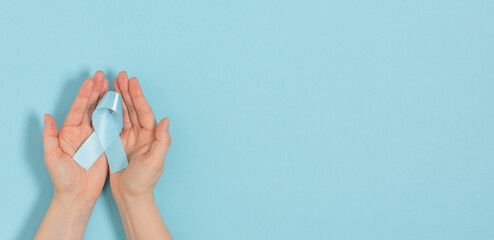  Woman hands holding blue ribbon, as a symbol of diabetes over blue pastel background.