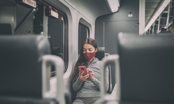Train passenger using mobile phone during travel commute wearing face mask for coronavirus pandemic. Panoramic banner of people lifestyle commuting after work at night.