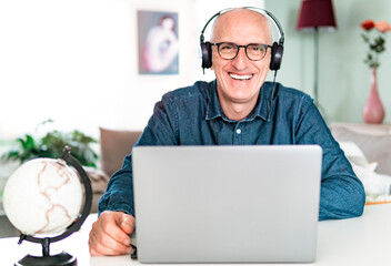 Smiling business man looks into camera wearing headphones - businessman on video call manages work from home to home - remote working concept