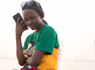 Young beautiful black girl using smart phone on sea at sunset