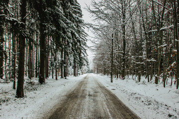 Dangerous stretch of road covered with snow and ice.Snowy road through forest.Winter panorama.Driving in icy frozen landscape.Bad weather conditions.Slippery asphalt road.Weather forecast scene