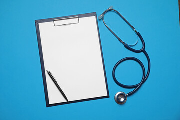 Clipboard, stethoscope and pen on light blue background, flat lay