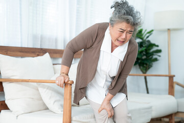Senior Asian woman suffering from knee pain at home.